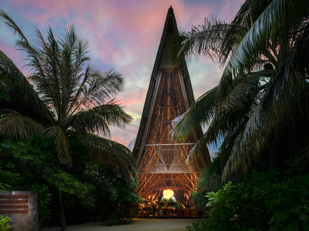 Mövenpick Resort Kuredhivaru, ONU Marché tall A-frame thatched-bamboo pavilion at dusk, Noonu Atoll, Maldives