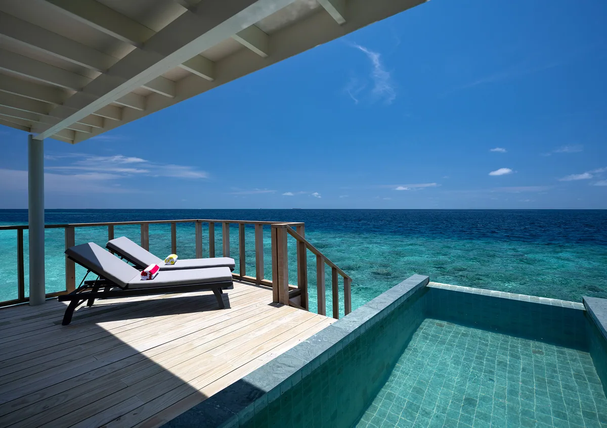 OBLU SELECT Lobigili, villa overwater, North Malé Atoll, Maldives, Water Villa with Pool private deck configuration: timber decking with two recessed loungers (rolled towels with flower garnish), glass-tiled plunge pool flush with deck edge, the reef bowl and open lagoon stretching to the horizon.