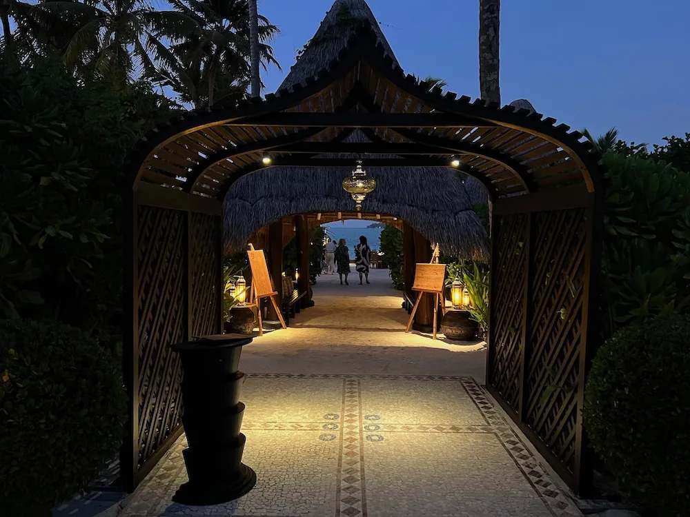 Restaurant entrance at dusk with thatched-tunnel walkway, Moroccan hanging lantern and mosaic floor at One&Only Reethi Rah.