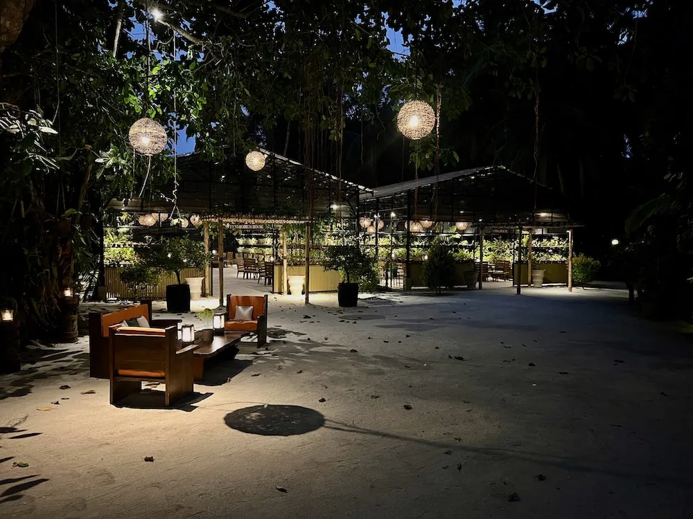 Outdoor evening dining patio under tree canopy with hanging woven globe lanterns and wooden lounger seating at One&Only Reethi Rah.