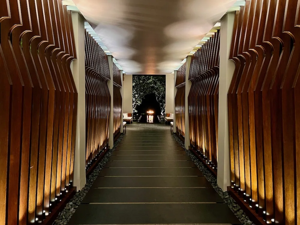 Curved-slat wooden tunnel walkway leading to a fire-lit lounge at One&Only Reethi Rah, Cheong Yew Kuan architectural signature.