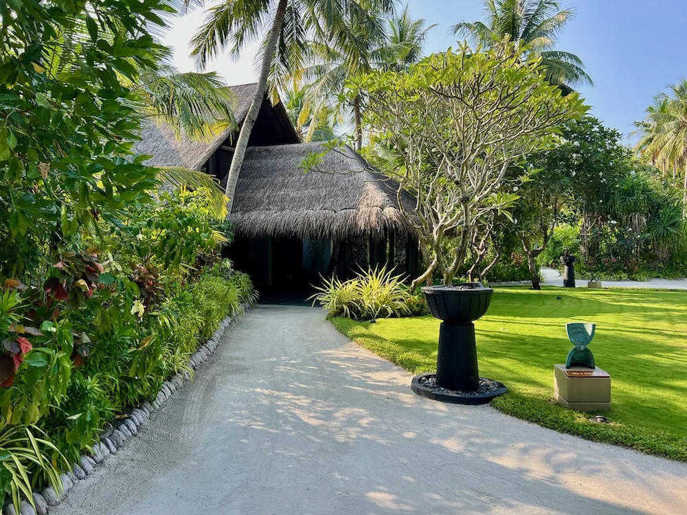 ESPA pavilion exterior with A-frame thatched roof and frangipani tree in garden approach at One&Only Reethi Rah.