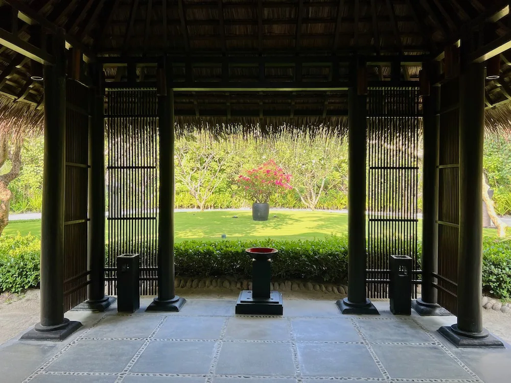 Spa pavilion interior with Asian-temple-style dark wood pillars and thatched ceiling, view through to garden bonsai at One&Only Reethi Rah.