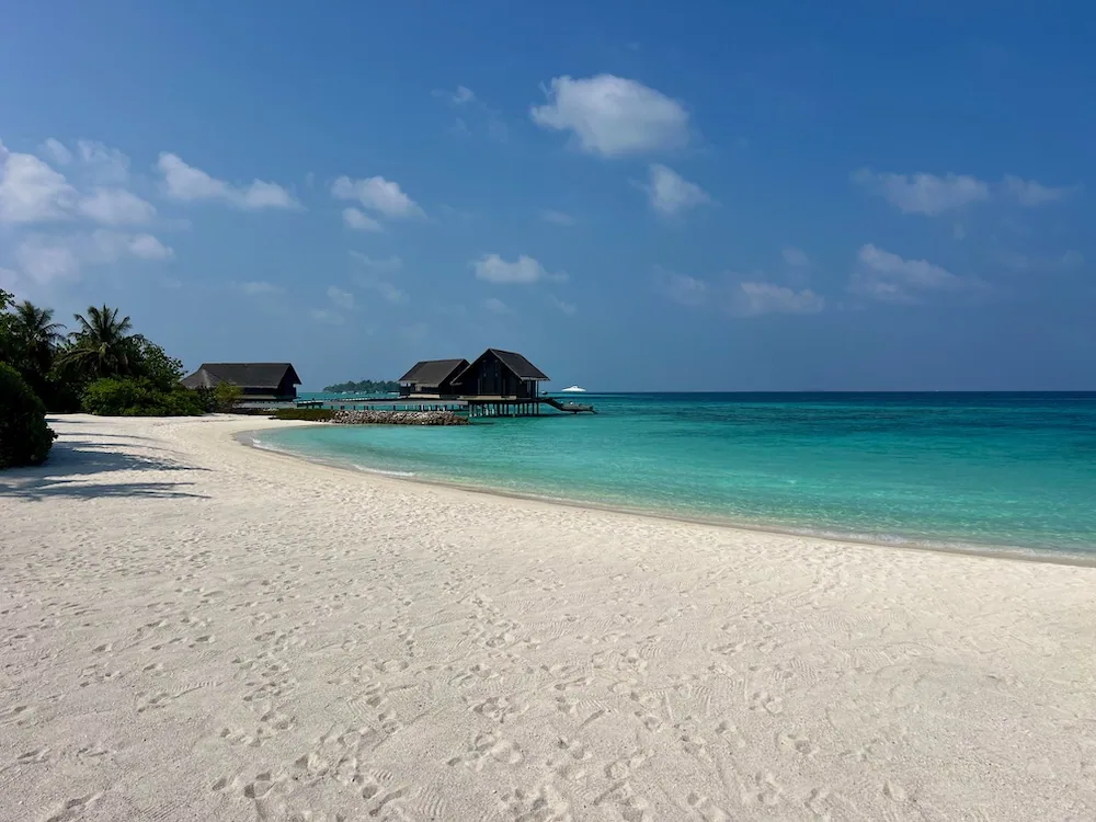 Curving white-sand beach with distant over-water pavilions over turquoise lagoon at One&Only Reethi Rah.