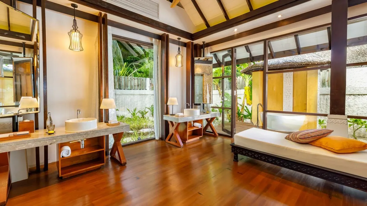 OZEN RESERVE BOLIFUSHI, spa, South Malé Atoll, Maldives, ELE NA Spa double-treatment vanity: twin trestle-wood vanities with vessel sinks, framed mirrors with pendant lamps overhead, a side daybed with mustard pillows for post-treatment lounging, sliding doors opening onto a green garden screen.