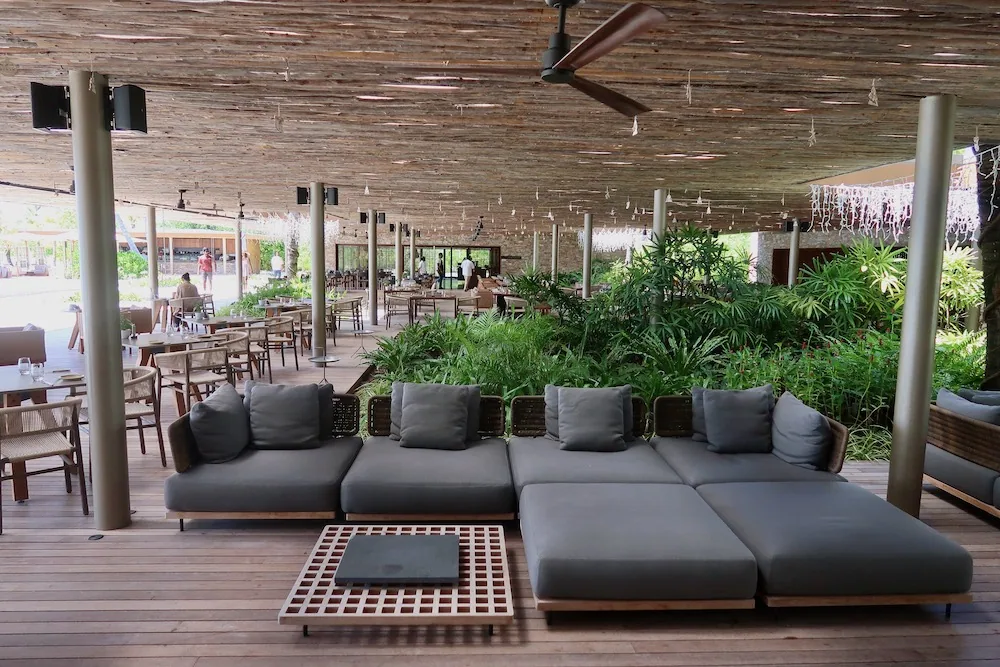 Patina Maldives, Fari Islands, dining, North Malé Atoll, Maldives, Portico restaurant interior, the open-air sand-floor pavilion with travertine pillars, low timber tables and woven cane chairs, the resort's all-day venue running from breakfast through the early-evening rotation.