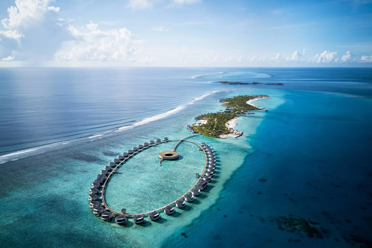 The Ritz-Carlton Maldives, Fari Islands, aerial, North Malé Atoll, Maldives, The Ritz-Carlton Maldives Fari Islands drone aerial showing the signature circular over-water villa ring around the central spa pod, the connecting jetty to the main palm-covered island with beach pool villas, reef-edge breaking surf at the outer rim, North Malé Atoll.