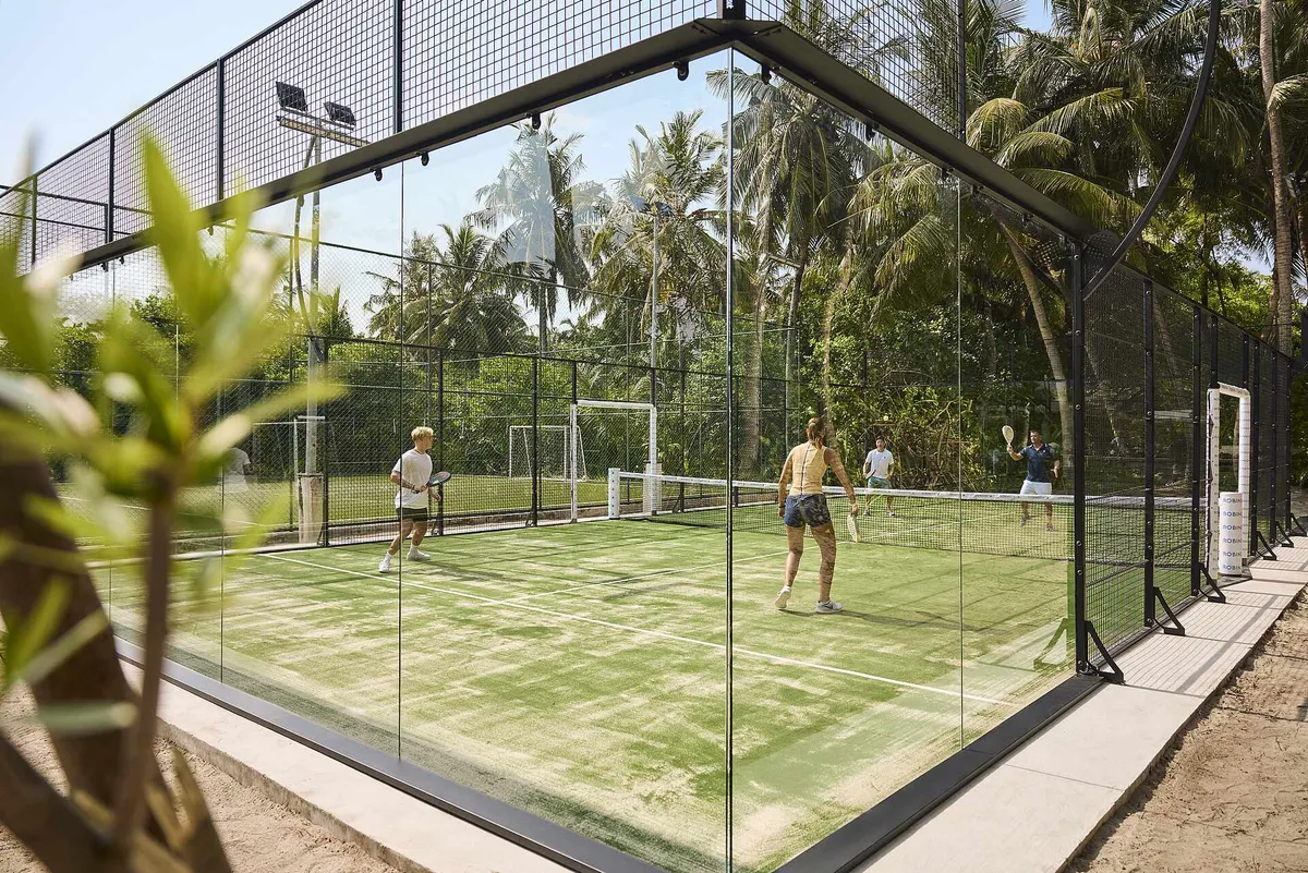 Robinson Club Noonu, glass-walled padel courts with four players on green turf surrounded by palm forest, Noonu Atoll, Maldives