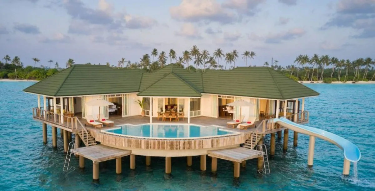 Siyam World Maldives, Two Bedroom Overwater Villa with Pool and Slide at dusk, central infinity pool open to lagoon, blue curved waterslide on south flank, Noonu Atoll, Maldives