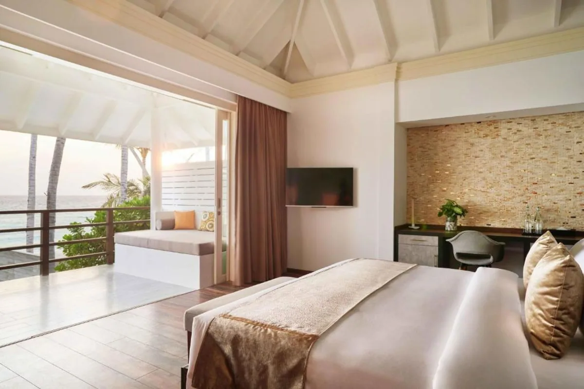 Siyam World Maldives, Beach Villa bedroom with vaulted exposed-beam ceiling, copper-trim king bed, woven straw wall feature and private balcony to ocean, Noonu Atoll, Maldives