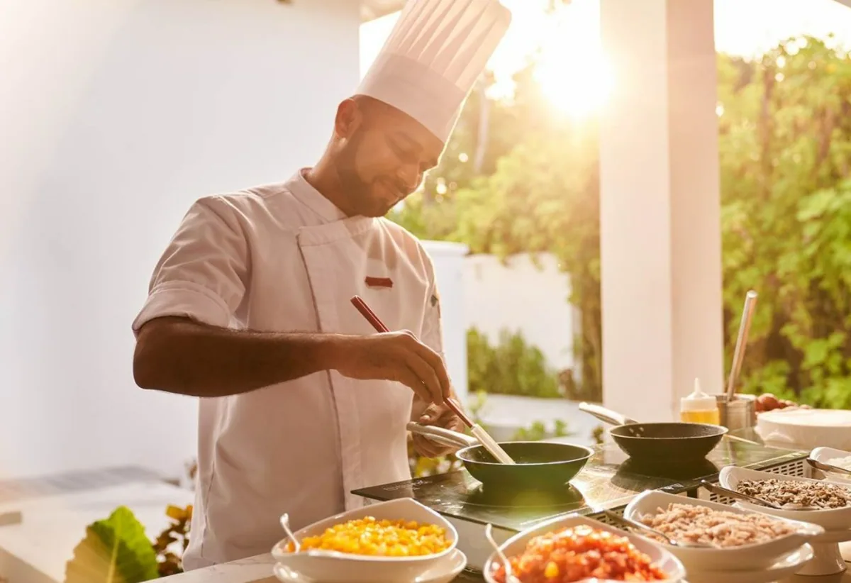 Siyam World Maldives, Baraabaru international venue chef at live cooking station with sweetcorn, tomato salsa and tuna prep bowls under sunset palm light, Noonu Atoll, Maldives