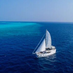 Soneva in Aqua chartered yacht moored over turquoise Baa Atoll water under blue sky.