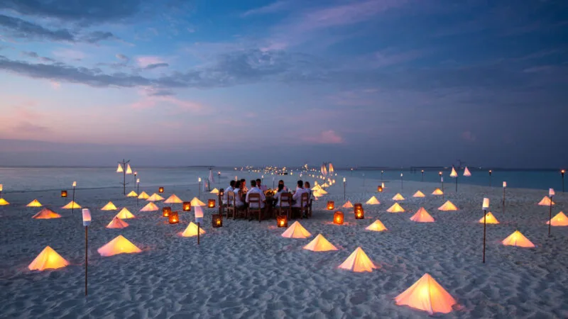 Private sandbank dinner table set for two against a soft sunset off Soneva Fushi, Baa Atoll.