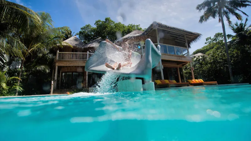 Family beach villa with red waterslide from pool deck into the lagoon at Soneva Fushi.