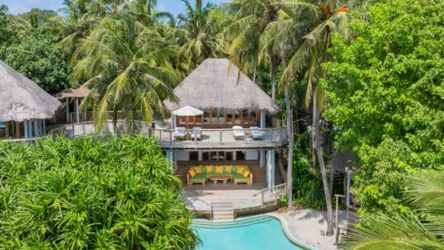 Three-bedroom Jungle Reserve villa with thatched roof and sand-floor pool under dense banyan canopy at Soneva Fushi.