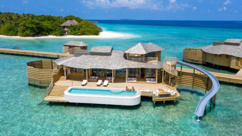 Floating wooden breakfast tray with fruit and pastries in a villa pool over turquoise water at Soneva Fushi.