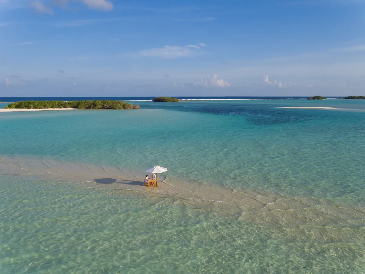 Dining in Water table set inside the shallow lagoon at Soneva Jani, guests seated with feet in the water.