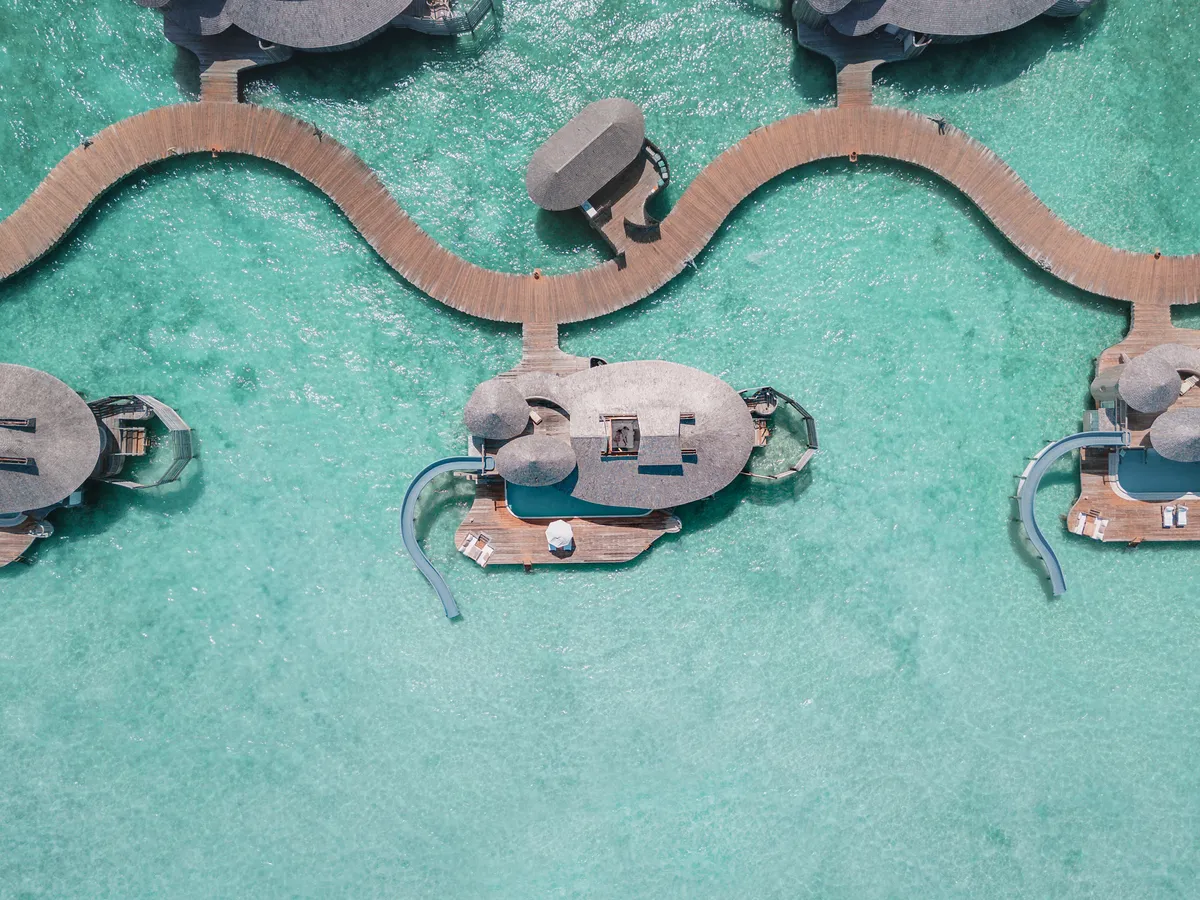 Aerial of Soneva Jani over-water villa cluster with one villa's retractable roof open showing the bedroom below.