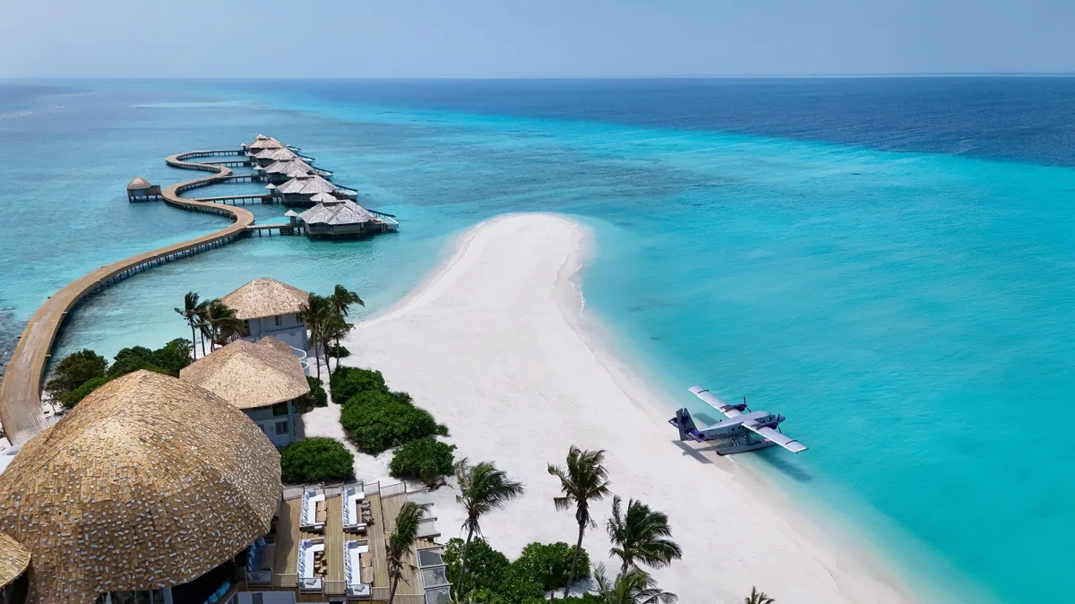 Soneva Secret, aerial, Haa Dhaalu Atoll, Maldives, Soneva Secret aerial: a Twin Otter seaplane parked on the sandbank with the thatched-roof overwater villa cluster ringing the lagoon edge, signature Soneva seaplane-arrival framing.