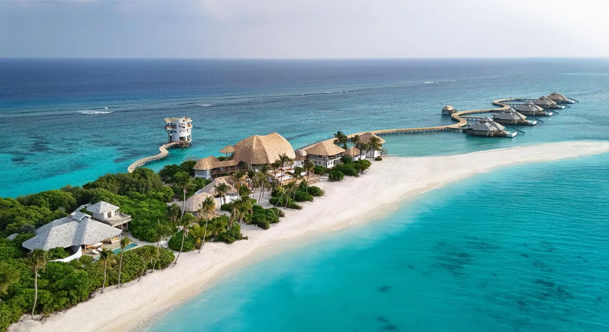 Soneva Secret, aerial, Haa Dhaalu Atoll, Maldives, Soneva Secret establishing aerial: the white Out of This World observatory tower above the lagoon, the Crusoe Island villas tucked into the island vegetation, the overwater jetty line at the right edge.