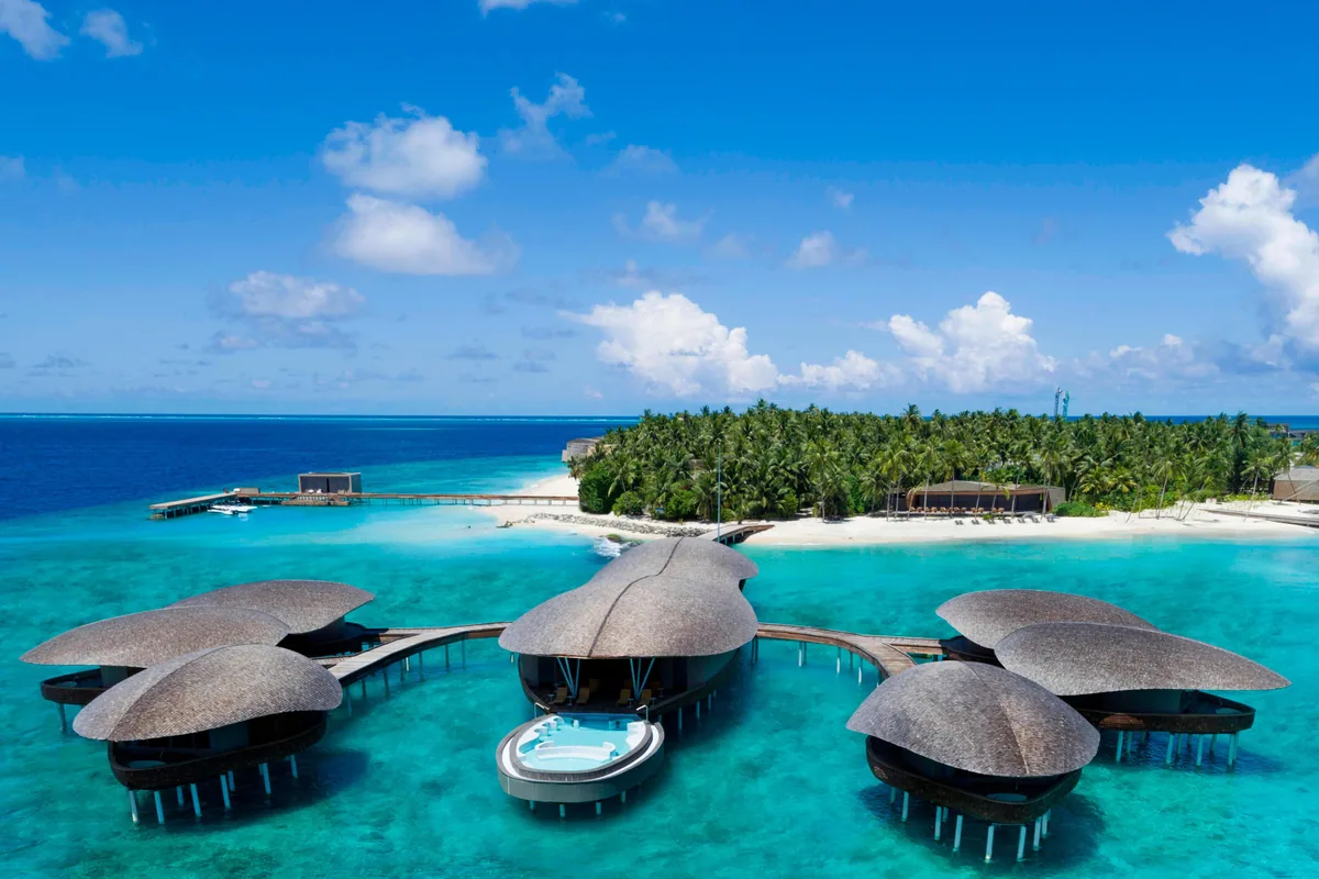 The St. Regis Maldives Vommuli Resort, spa, Dhaalu Atoll, Maldives, Iridium Spa aerial: six thatched-roof spa pavilions in a circular half-moon clam-shell arrangement around a central round plunge pool, detached from the main island in the lagoon and connected by boardwalks. The country's most-photographed St. Regis architectural feature internationally.