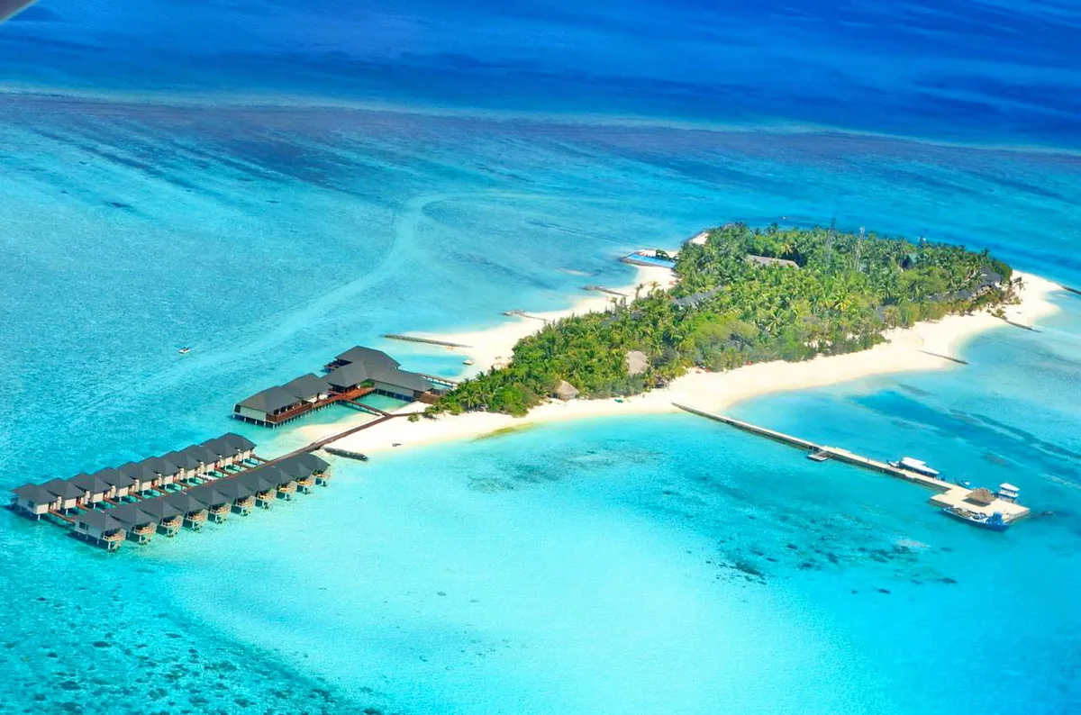 Summer Island Maldives, aerial, North Malé Atoll, Maldives, Full-island wide aerial: the elongated Ziyaaraifushi island geometry with the pyramid-roof overwater villa row extending from the left side along its perpendicular jetty, central palm-canopied island with the main pavilion building visible, T-shaped arrival jetty at the right with speedboat moored, sandbank at the eastern tip.