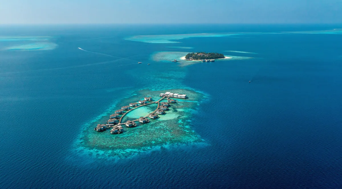 The Halcyon Private Isles Maldives, aerial, Gaafu Alifu Atoll, Maldives, Halcyon two-island concept aerial, the main island (background) and the separate over-water villa oval cluster on a dedicated reef-flat (foreground), reef gradient from turquoise shallows to deep navy ocean.