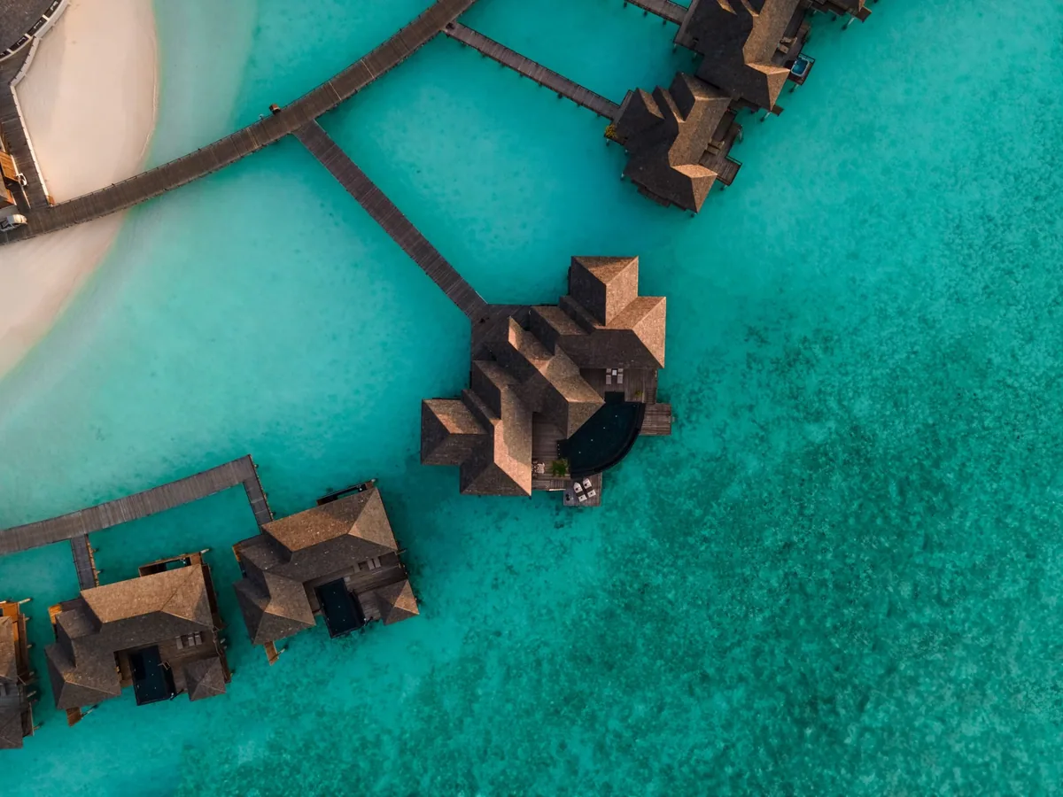 Sun Siyam Iru Fushi, top-down drone aerial of pyramid-roof Infinity Water Villa cluster with boardwalk geometry on reef shelf, Noonu Atoll, Maldives