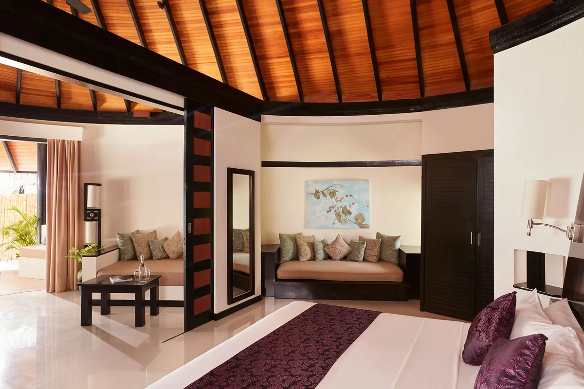 Sun Siyam Iru Fushi, Family Beach Villa interior with domed red-stained wooden ceiling, king bed with aubergine throw, banquette seating and dark wood floor, Noonu Atoll, Maldives