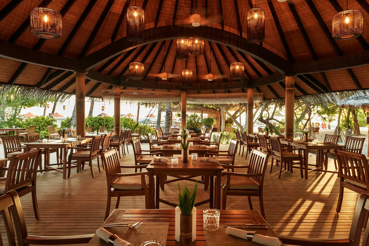 Sun Siyam Iru Fushi, Bamboo Asian pavilion with bell-shaped rattan pendants, wooden tables and chairs on deck under thatched roof with ocean beyond, Noonu Atoll, Maldives