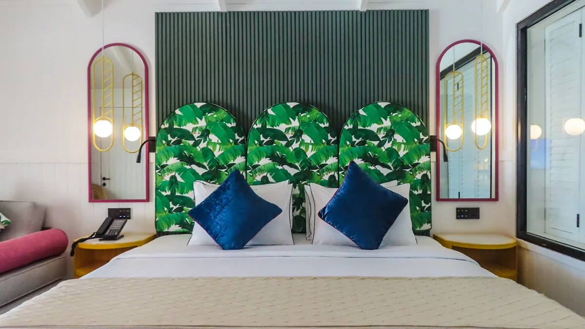 Villa Park Sun Island Resort, villa beach, Alif Dhaal (South Ari) Atoll, Maldives, Vibrant Villa bedroom with the distinctive triple-arch headboard panels in banana-leaf print, the vertical dark-green slat feature wall, twin pink-framed arched mirrors with brass globe sconces, and navy velvet pillows on the king bed.