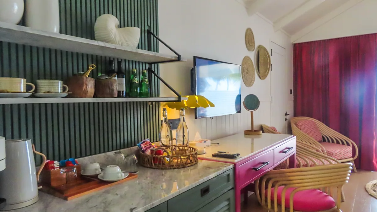 Villa Park Sun Island Resort, villa beach, Alif Dhaal (South Ari) Atoll, Maldives, Vibrant Villa minibar and dressing alcove with the green-slat-back open shelving, the Carrara-marble counter, the pink rattan armchair pair, fuchsia drape, magenta dressing table with brass-handle drawers, and yellow petal sconce.