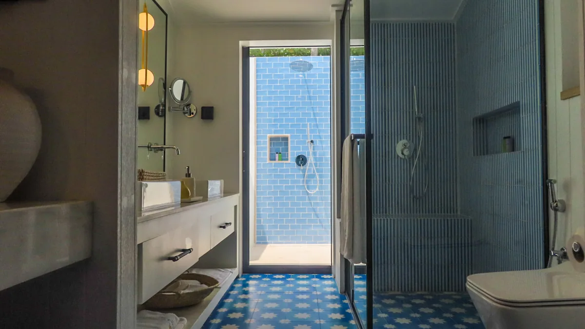 Villa Park Sun Island Resort, villa beach, Alif Dhaal (South Ari) Atoll, Maldives, Vibrant Villa bathroom alternate with the Moroccan-pattern blue-and-white star-tile floor, the wall-mounted vanity with woven-basket storage, the indoor-outdoor shower opening to blue subway-tiled rinse area, and the rain shower glass enclosure.