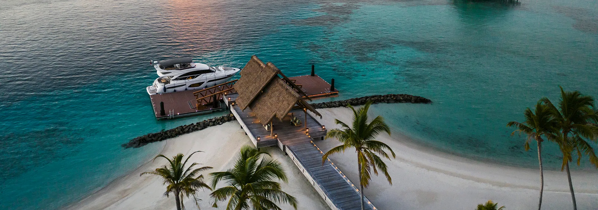 Waldorf Astoria Maldives Ithaafushi, arrival, South Malé Atoll, Maldives, Waldorf Princess yacht docked at the Private Island arrival jetty at golden hour, thatched welcome pavilion and palm-fringed white sand beach setting the 40-minute transfer apart from the seaplane-only norm.
