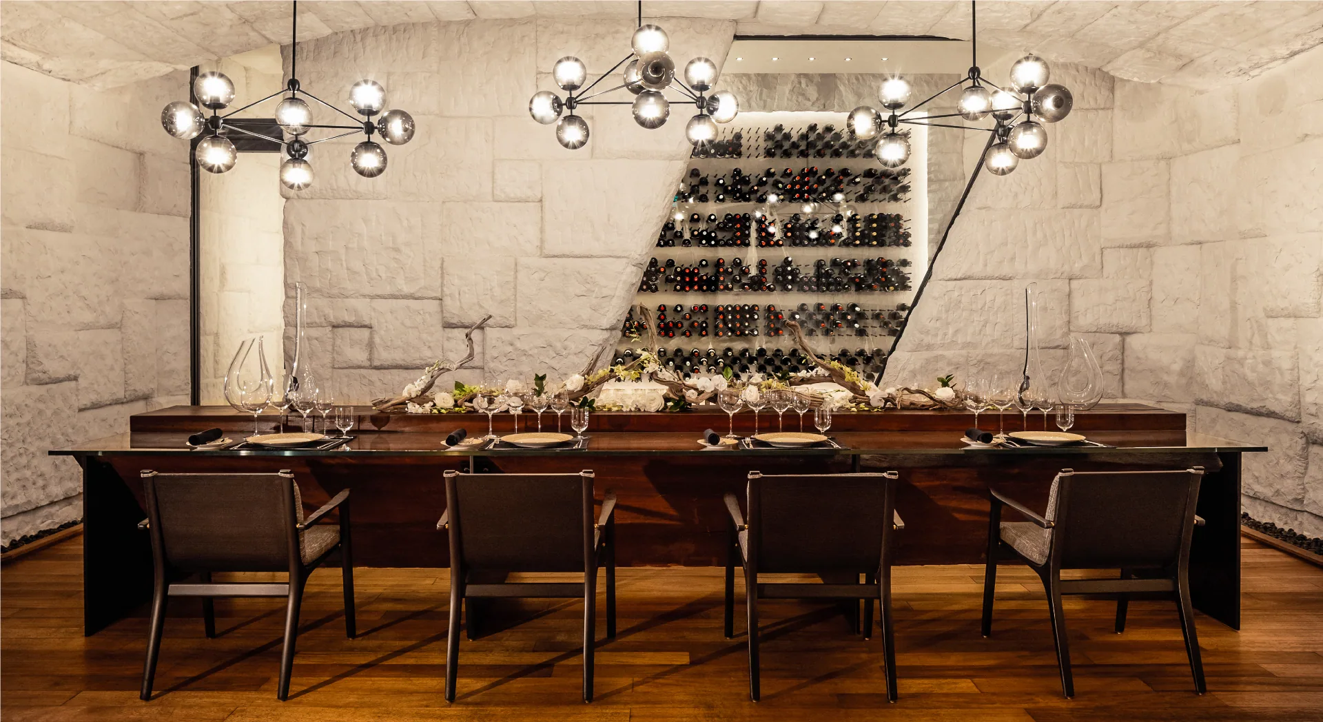 Waldorf Astoria Maldives Ithaafushi, dining, South Malé Atoll, Maldives, The Rock, Jordanian-limestone cave dining room, illuminated angled wine wall and the 200-year-old Jarrah wood table flanked by black globe chandeliers and leather chairs.