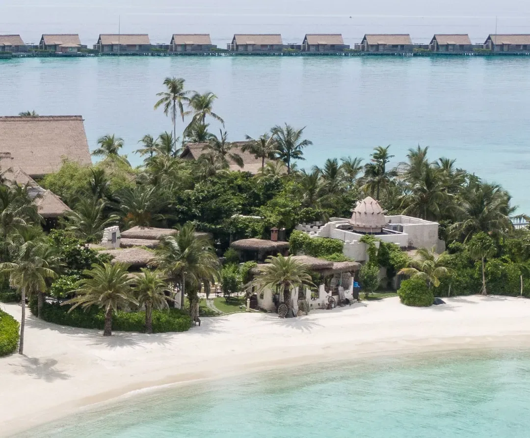 Waldorf Astoria Maldives Ithaafushi, dining, South Malé Atoll, Maldives, Yasmeen Levantine restaurant, whitewashed Syrian-village walls and small dome on the beach, palm trees and the overwater villa line stretching into the lagoon behind.