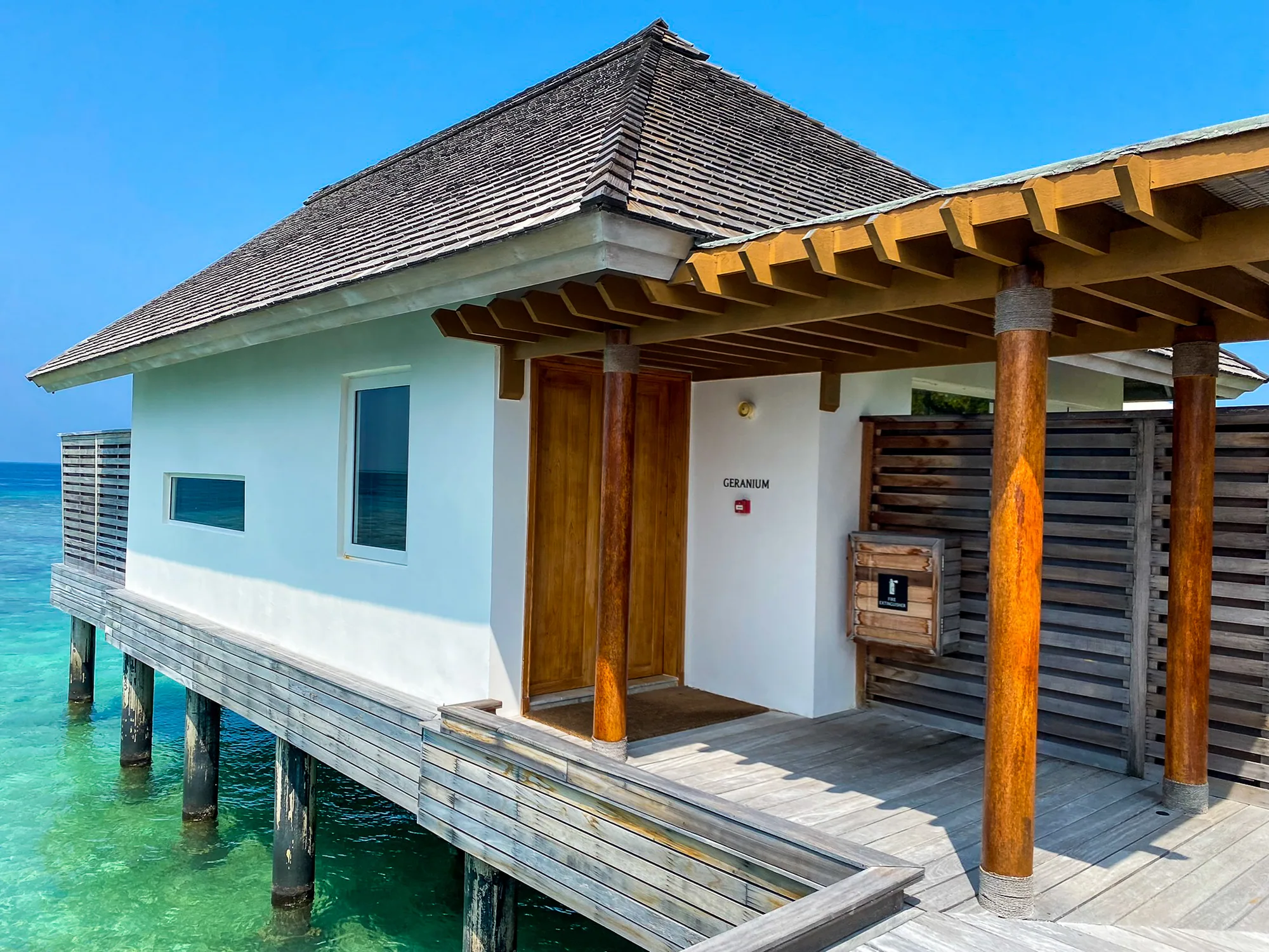 Waldorf Astoria Maldives Ithaafushi, spa, South Malé Atoll, Maldives, Overwater spa treatment villa Geranium, one of the botanical-named single-villa cabins on the spa boardwalk, pitched shingle roof and timber-column verandah over the lagoon.